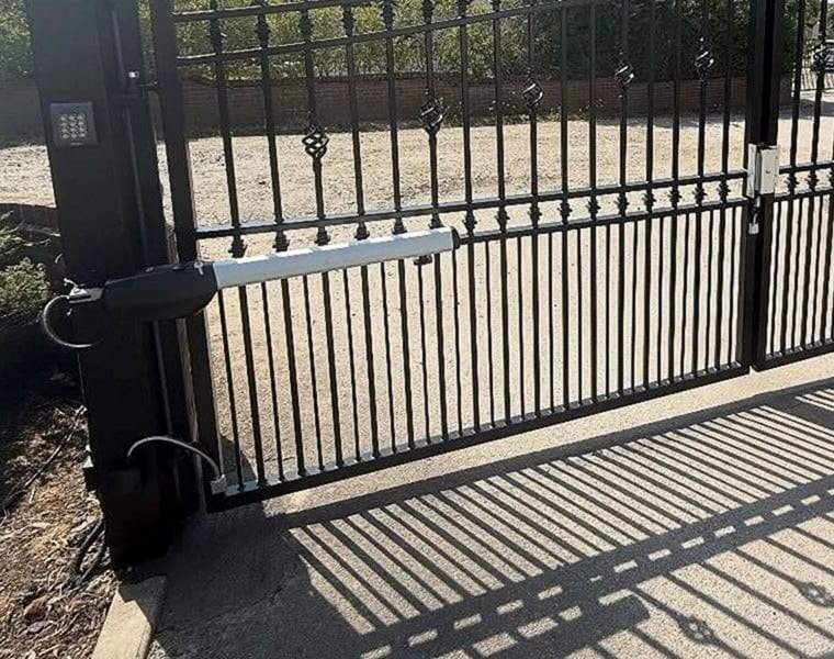 Swing gate operator arm on the hinge post of a black ornamental driveway gate, with a keypad mounted on the post