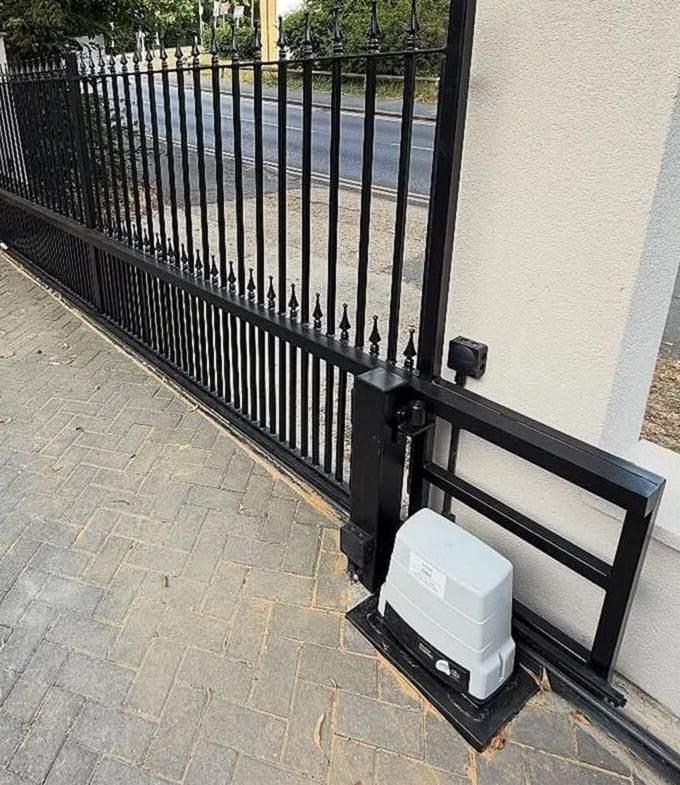 Slide gate operator on a concrete pad at the end of a black spear-top slide gate, with its guide frame